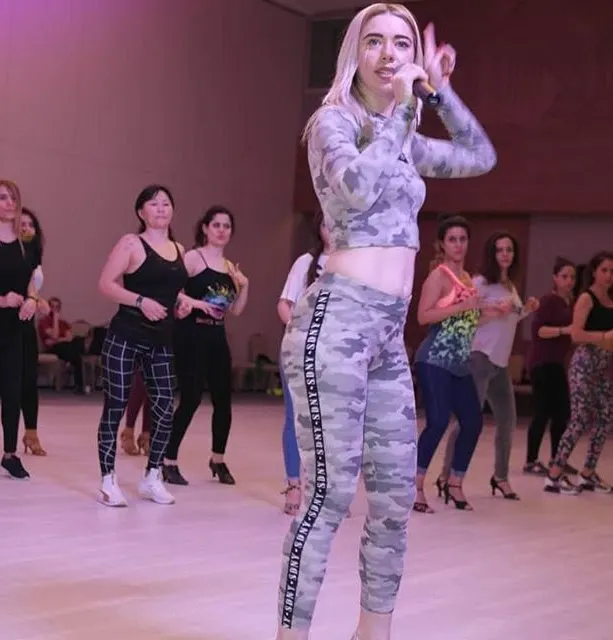 Anna Borovska leading a Bachata Solo class with a microphone while a room of dancers follows along